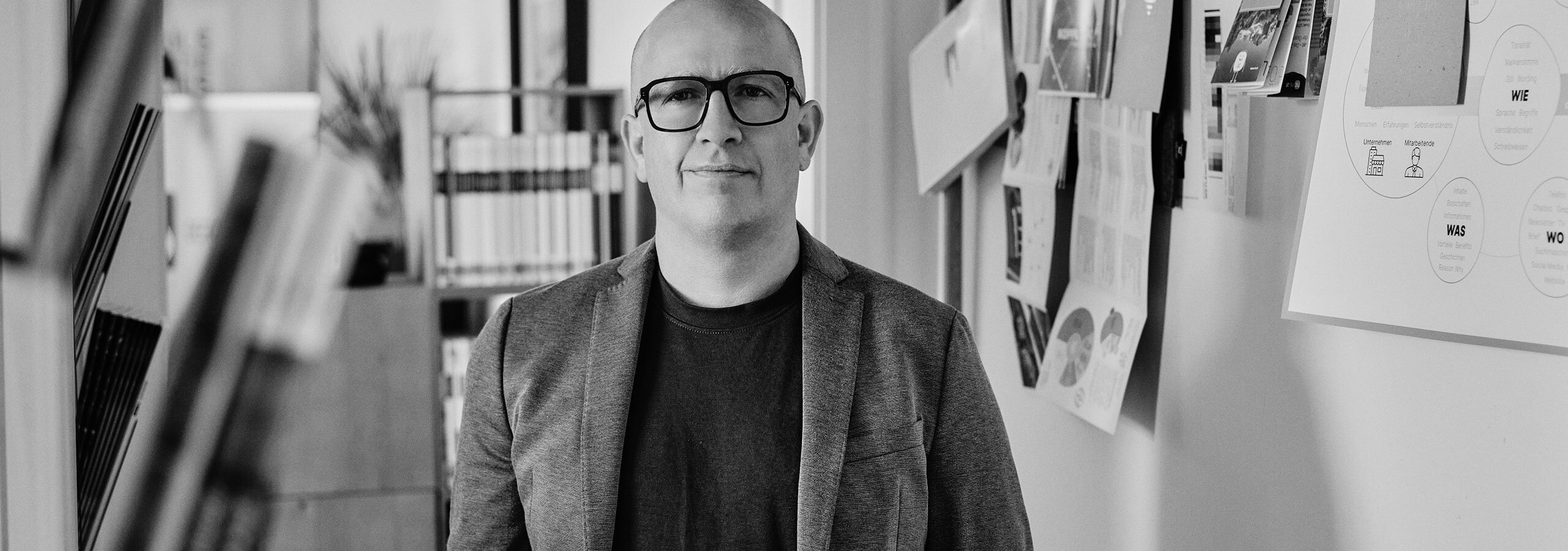 Horst Köpfelsberger steht im Ganz vor dem Portfolio seiner Printprojekte im Gang der Agentur designkraft
